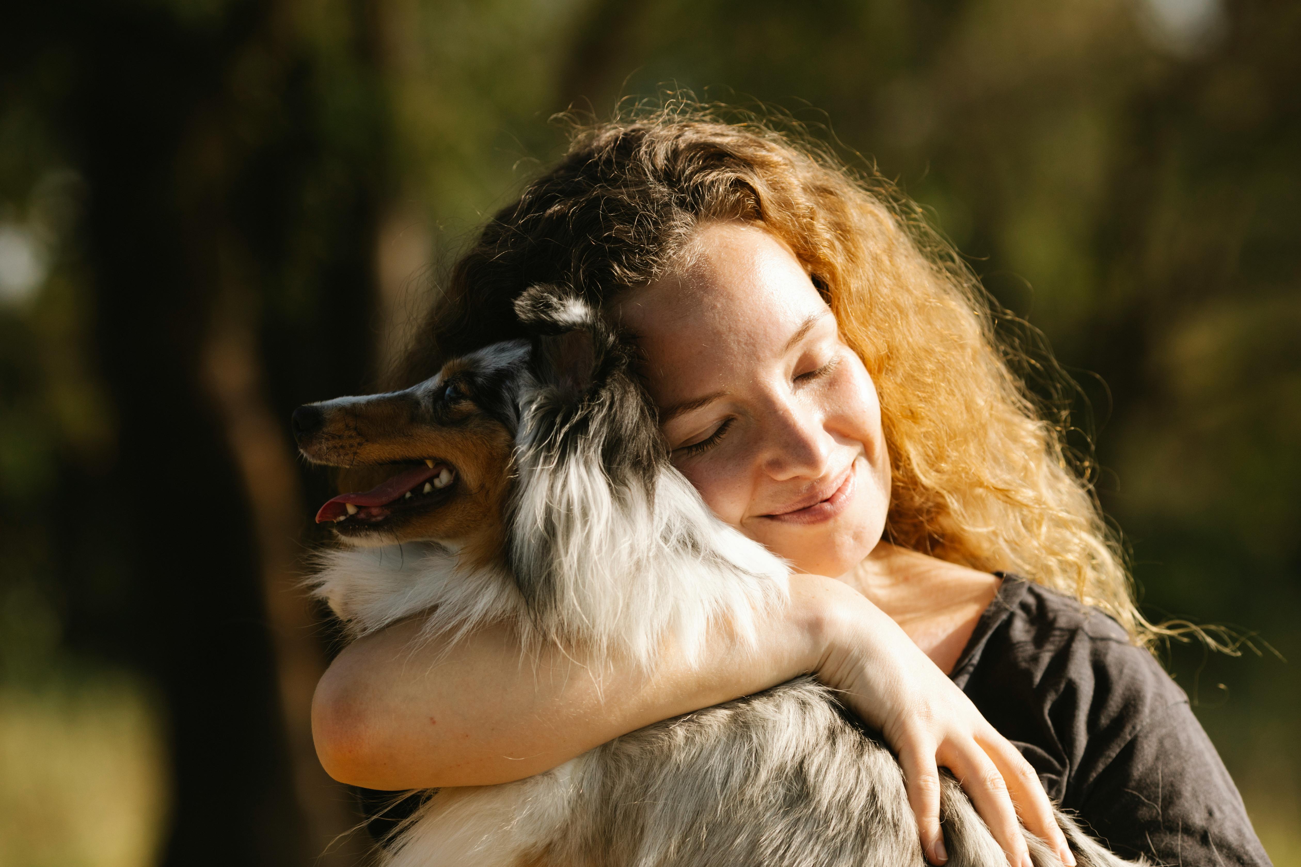 Woman hugging an Australian Shepherd dog with a blurred natural background